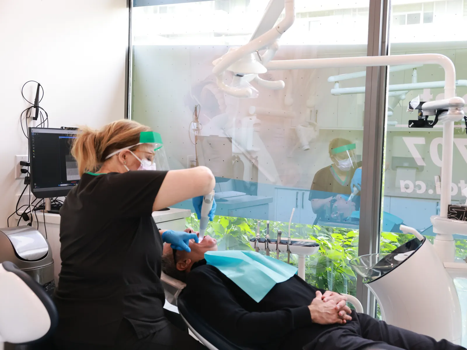 Hygienist performing a preventive dental cleaning in a bright treatment room with garden views