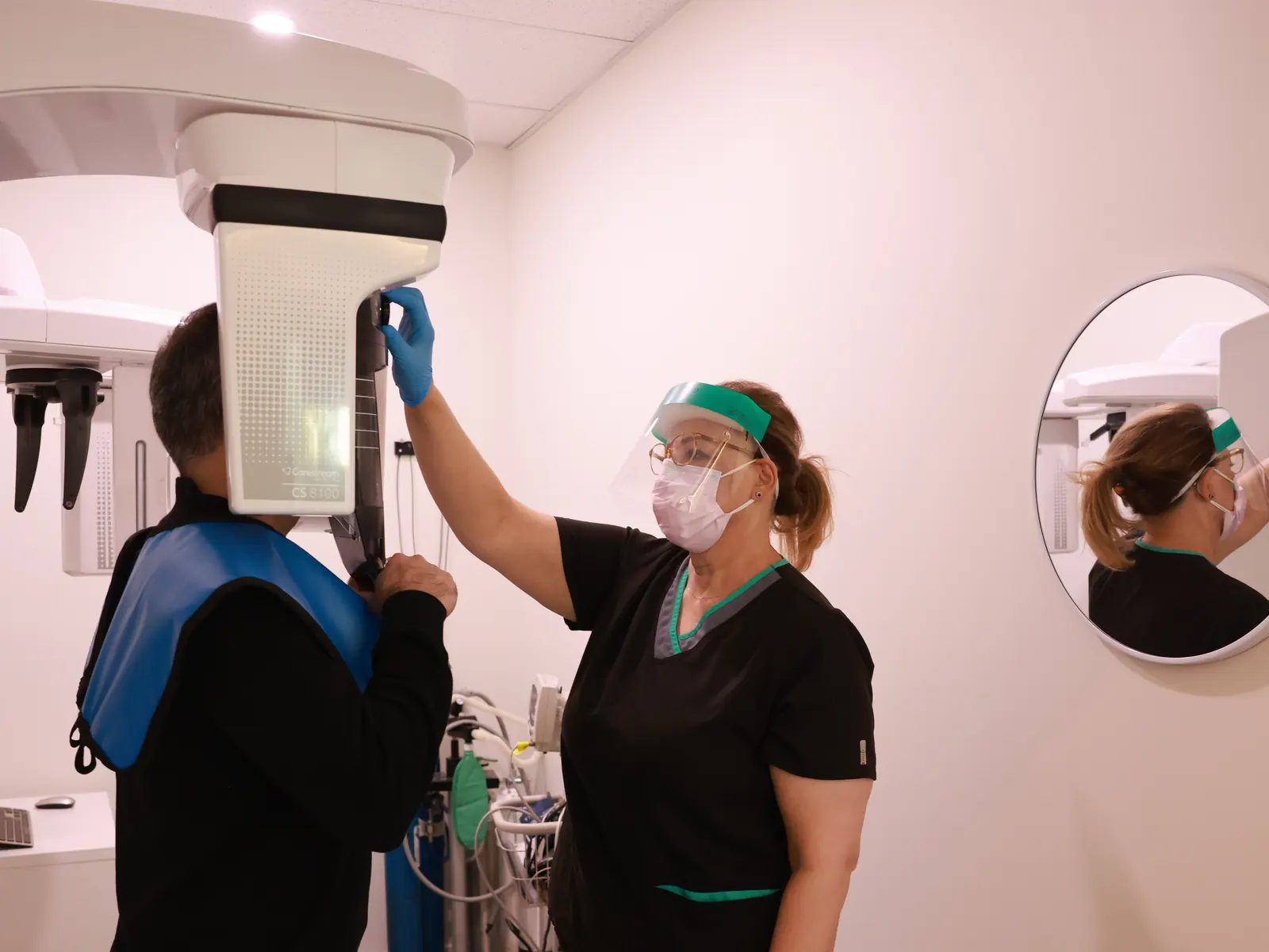 Team member positioning a patient in a panoramic dental X-ray machine with a protective lead apron