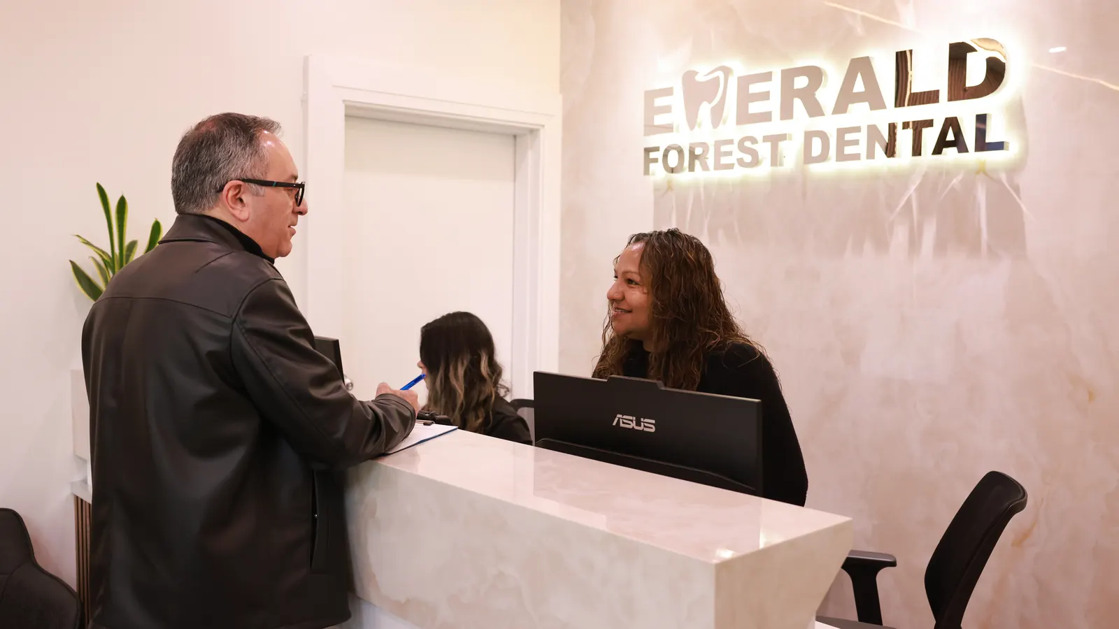A patient checking in with front-desk staff at the marble reception counter of Emerald Forest Dental Clinic