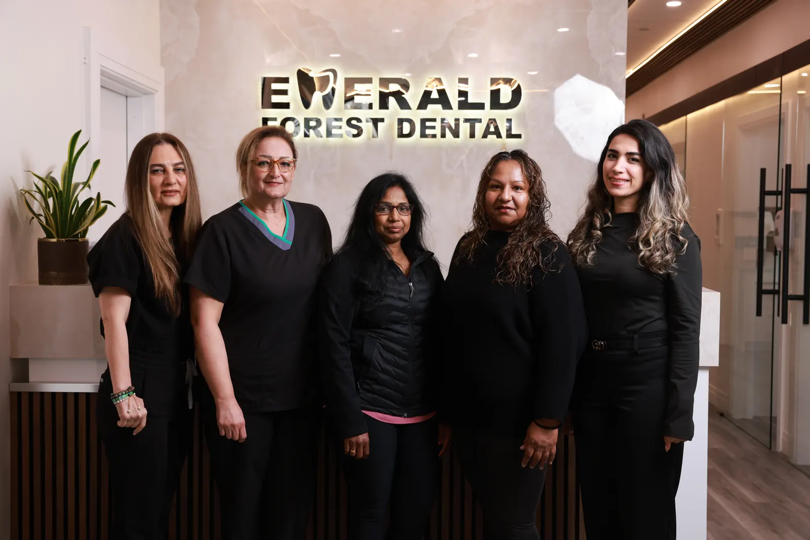The Emerald Forest Dental Clinic team in black scrubs standing together in front of the clinic's illuminated reception sign